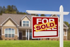 A Sold sign is in clear view in front of a house that is blurred in the background. 